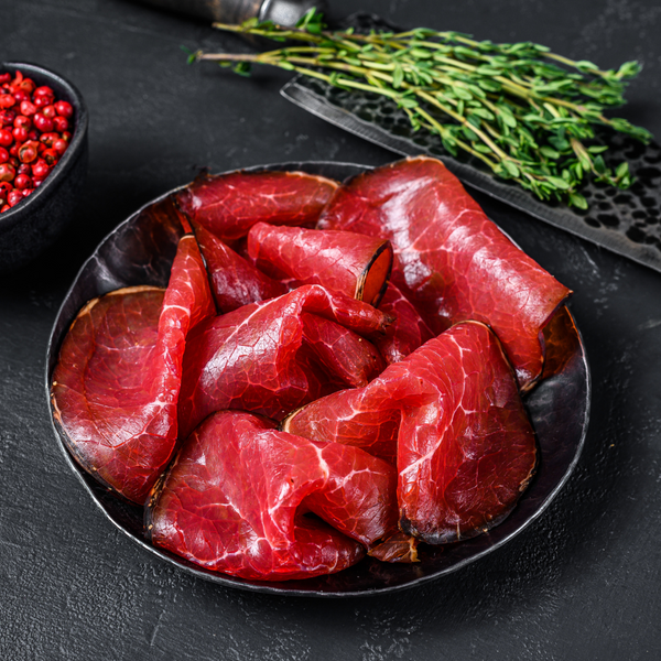 Beef bresaola sliced displayed on wood board, ready-to-eat Italian cured meat, deep red color with white fat marbling, 250g pack