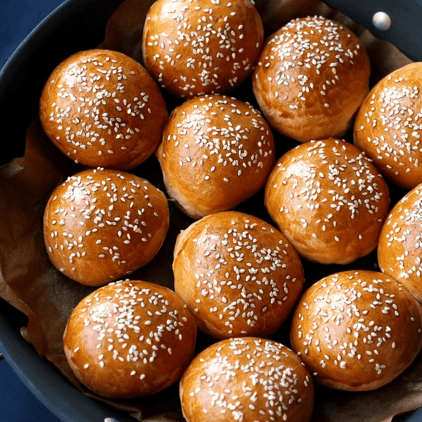 Freshly baked artisan brioche burger bun sliders, golden-brown with sesame seeds, perfect for gourmet mini burgers