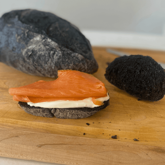 Freshly baked artisan bread with activated charcoal, featuring a dark crust and rustic texture on wooden surface