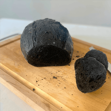 Artisan bread with activated charcoal, freshly baked loaf with dark appearance and rustic texture on wooden surface
